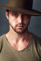 Portrait, serious and man with hat, studio and stylish with clothes, cool and calm in fashion week. Confident, face and person with tshirt for runaway, model and creativity in grey background in USA