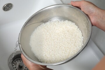 Wall Mural - Woman rinsing rice in bowl above sink, closeup