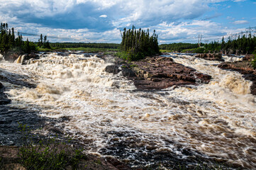 Capturing the wild spirit of Rivière aux Rochers, this photo reveals tumultuous rapids swirling among craggy rocks, surrounded by lush boreal forest.