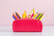 © prime1001 - Back to school concept. Pink full pencil case with pencils and pens, scissors, school supplies isolated on against background of pink wall with empty space.