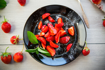 Wall Mural - fresh fruit salad of ripe strawberries on a light wooden table