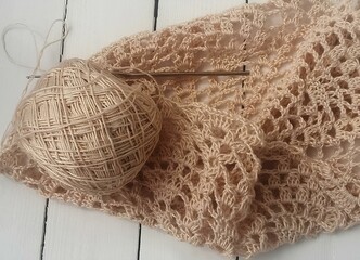 a ball of beige or light brown yarn and a crochet hook resting on a partially completed crochet project. The crochet work appears to be a lace pattern, with intricate openwork that creates a delicate 