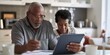 © Iryna - An elderly black couple deals with bills and mortgage planning together using a laptop in their kitchen.