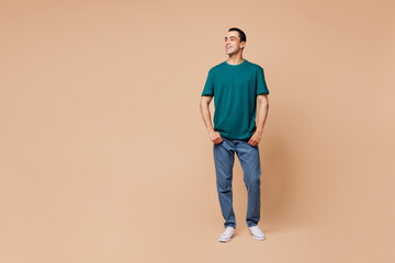 Wall Mural - Full body young smiling fun happy cheerful middle eastern man wear blue t-shirt casual clothes look aside on area mock up isolated on plain pastel beige background studio portrait. Lifestyle concept.