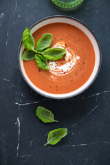 Wall Mural - Roasted tomato and red bell pepper soup served with yogurt and green basil, vertical shot on a black marble background with space, above view