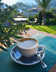 Serene scene with coffee cup on saucer, outdoor cafe table, green landscape. Morning breakfast drink