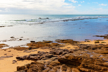 Wall Mural - Ocean is calm and the rocks are scattered across the beach. The sky is cloudy and the water is a deep blue color