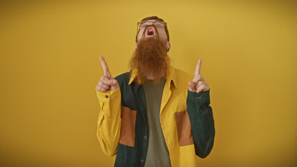 Wall Mural - Bearded redhead man pointing upwards isolated over yellow background wearing glasses.