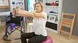 © Krakenimages.com - A young blonde woman exercises with dumbbells while sitting on a balance ball in a physical therapy clinic.