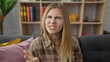 © Krakenimages.com - A young blonde woman appears annoyed in a cozy home setting, seated on a sofa with furnishing and bookshelf backdrop.