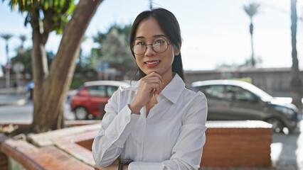 Canvas Print - Smiling asian woman in glasses outdoors in a city park with cars and trees in the background.