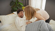 © Krakenimages.com - A woman tickling a smiling man on a comfortable bed in a cosy bedroom, depicting playfulness and intimacy.