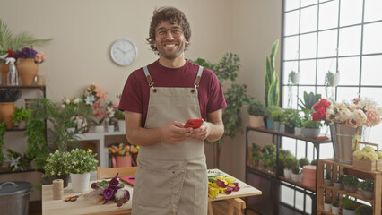 Sticker - A cheerful man with glasses and beard in an apron holding a phone in a flower shop full of various plants.