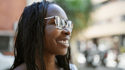 Wall Mural - Smiling african american woman with curly hair wearing glasses outdoors in the city.