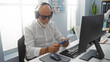 © Krakenimages.com - Senior man with grey hair and beard wearing headphones and using mobile phone in modern office indoors