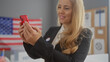 © Krakenimages.com - A young blonde woman in a suit smiles while using a smartphone in an indoor electoral college setting with an american flag.