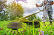 © Vladimir Razgulyaev - Man using a grass trimmer to cut the lawn in a vibrant, green garden. Active outdoor garden maintenance.