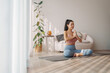 © eggeeggjiew - Contemplative Asian woman in lotus pose with hands in Namaste, tranquil morning yoga practice in home