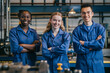 © 수동 김 - A group of three smiling, diverse workers in blue overalls standing arms crossed and looking at the camera with an industrial background