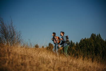 Wall Mural - Side view of a loving couple walking uphill and holding hands on a beautiful sunny day