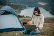 © La Famiglia - Female freelancer camping, sitting next to the tent, and having a video call on a laptop computer. digital nomad lifestyle