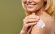 © Valerii Apetroaiei - A woman is smiling as she applies skincare cream on her shoulder