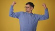 © procinemastock - Playful mature man with glasses showing off biceps against yellow background