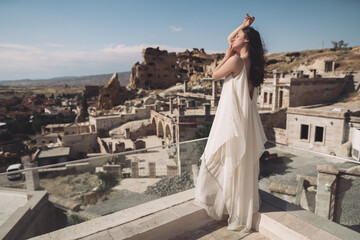 Wall Mural - A girl in a flying dress on the roof of a house on ancient city background.