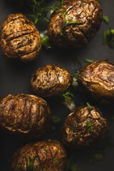 Wall Mural - Baked small potatoes with herbs on a black plate close-up.