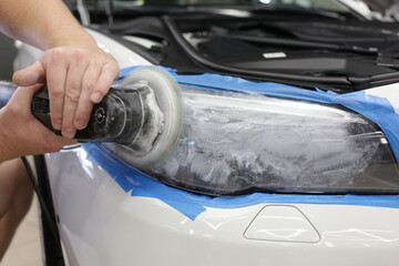 Cropped image of hands of male professional worker with orbital polisher in auto repair shop, polishing car headlight. Car wax polishing process. The process of polishing the headlights. 