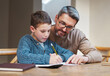 © peopleimages.com - Help, homework and dad with child at desk for teaching, learning and notebook for school project. Writing, notes and father studying in home with son for support, advice and growth in kids education