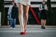 © qunica.com - Confident businesswomen walking in the city with focus on legs and red shoes. Professional attire emphasizing a dynamic city work environment.