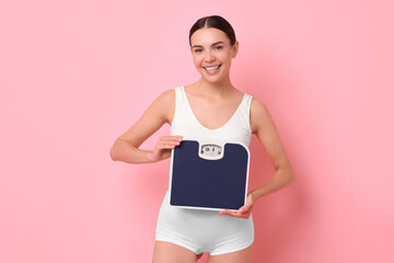 Poster - Diet and weight loss concept. Happy young woman with floor scale on pink background