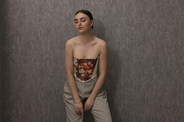 Wall Mural - Beautiful young woman in stylish corset near grey wall