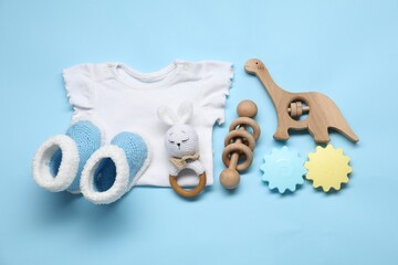 Canvas Print - Wooden rattles, baby shirt and knitted booties on light blue background, flat lay