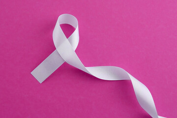 white awareness ribbon on pink background, top view