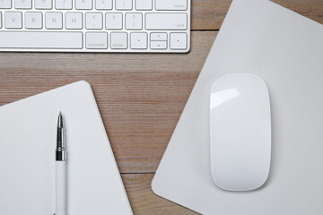 Wall Mural - Wireless mouse with mousepad, notebook, pen and computer keyboard on wooden table, flat lay