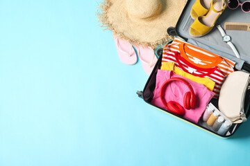 Wall Mural - Open suitcase with traveler's belongings on light blue background, flat lay. Space for text