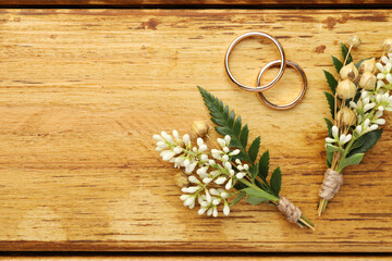 Wall Mural - Small stylish boutonnieres and rings on wooden table, flat lay. Space for text