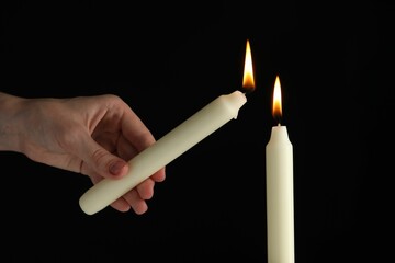 Wall Mural - Woman lighting candle on black background, closeup