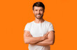 © Prostock-studio - A man smiles with his arms crossed while standing in front of an orange background.