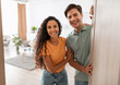 © Prostock-studio - Portrait of excited cheerful couple inviting guest friends to enter their home, happy young guy and lady standing in doorway of contemporary flat, millennial family holding door looking out together