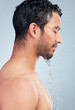 © peopleimages.com - Man, water and shower for body care in studio, bathroom and grooming on blue background. Male person, peace and liquid for skincare in profile, cosmetics and washing for hygiene or facial treatment