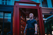 © qunica.com - Man standing outside a classic red telephone booth at night in an urban environment. Captures the aesthetic of city nightlife and modern style.