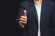 © meeboonstudio - Businessperson in suit giving thumbs up gesture on black background.