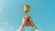 © KikkyCNX - Success concept. Champion golden trophy for winner is lifted up against blue sky representing achievement and successful hard work