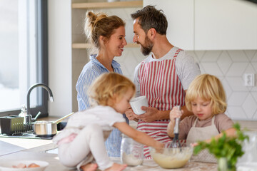 Wall Mural - Young nuclear family making pancakes together. Parents and children in kitchen, preparing pancake batter, spending weekend day indoors.