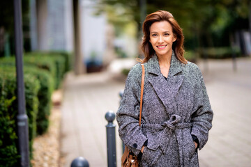 Wall Mural - Mid aged woman with brunette hair walking outdoor in the city street on autumn day