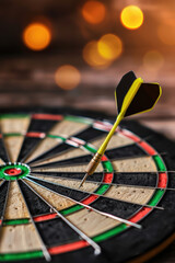 A close-up photo of a dart hitting the bullseye on a dartboard, with a blurred background and bokeh lights, symbolizing precision and success.