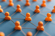 © tonstock - Interconnected orange figures representing a network of individuals on a blue background. Concept of communication, teamwork, and community.